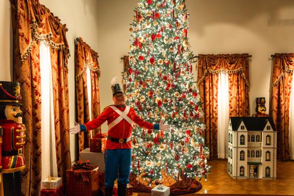 A nutcracker stands in front of a large decorated Christmas tree at the Nutcracker in the Castle exhibit at the Paine Art Center