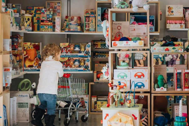 Young child pushing mini shopping cart through the aisles at Fat Brain Toys in Prairiefire