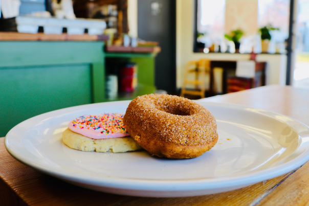 A cinnamon sugar donut and frosted sugar cookie sitting on a white plate in Mud Pie Bakery & Coffee