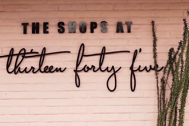 Image of a pink brick wall with "The Shops at Thirteen Forty Five" in black font