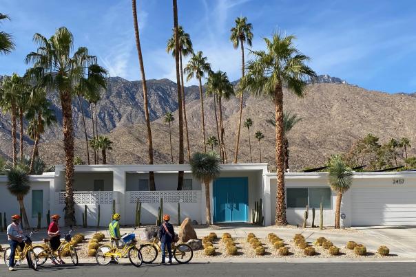 People are on their bike in front of a home in Palm Springs with the mountains in the background.