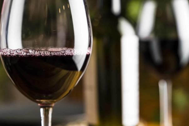 Wine tasting. A glass of red wine on the background of a restaurant table with bottle at an evening dinner or event party.