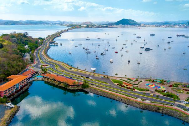 Aerial photograph of the Amador Causeway in Panama City, Panama, showing the causeway with bridge access, boats in the surrounding water, and a distant cityscape.