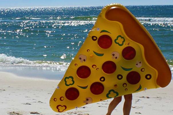 Person Walking Toward Beach Holding Large Inflatable Pizza Slice