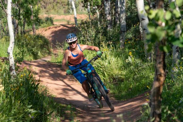 A female mountain biker rides a bermed trail through the woods at Woodward in Park City UT