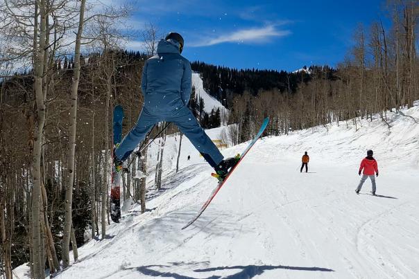A skier does a Spread Eagle of a small jump on a ski run at Park City Mountain