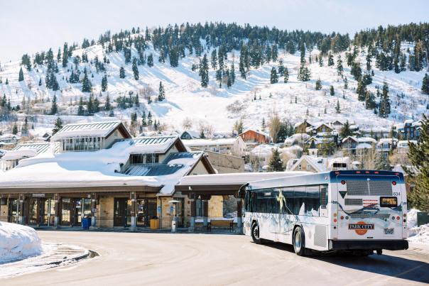 A bus pulls into the Old Town Transit Station in front of snowy ski runs in Park City, UT