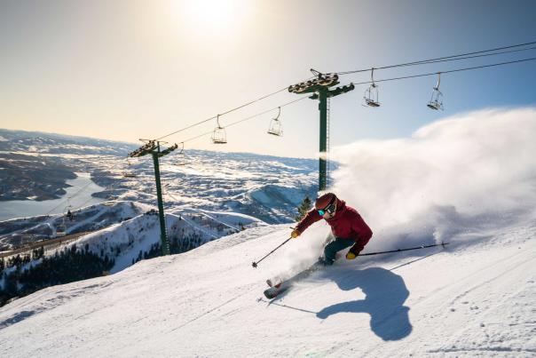 A skier carves a turn in front of a rising sun and chair lift at Deer Valley in Park City, UT