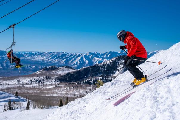 A skier drops into a ski run while skiers riding a chairlift look on in Park City, UT