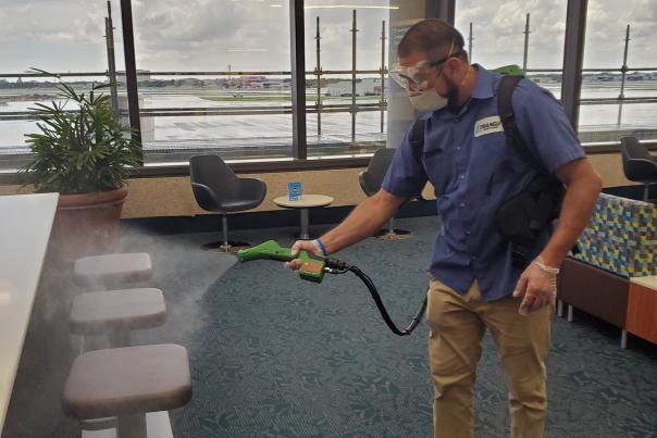 Janitorial team member uses electrostatic sprayer in the lounge area at PBI.