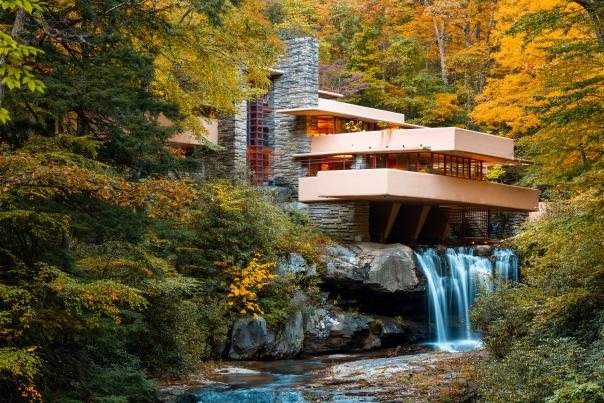 Iconic architectural building Fallingwater sits atop a waterfall with fall foliage surrounding.