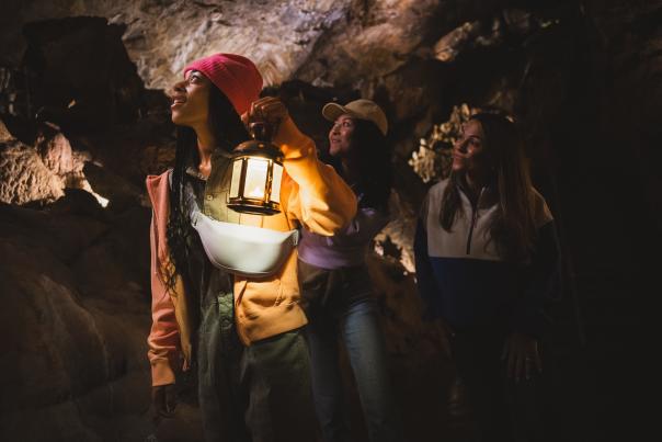 Three women, one with a lamp, exploring a dark, underground cave