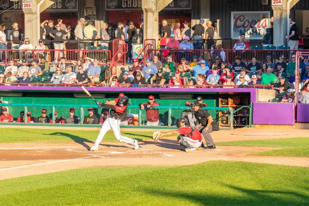 A baseball player swinging a bat in front of a dugout with people in the stands above