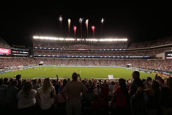 Fireworks blasting over a stadium at night filled with people