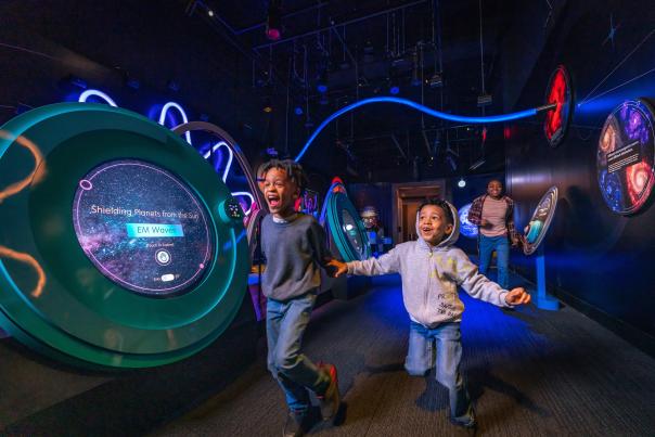 Two kids running around a dark display at the Franklin Institute