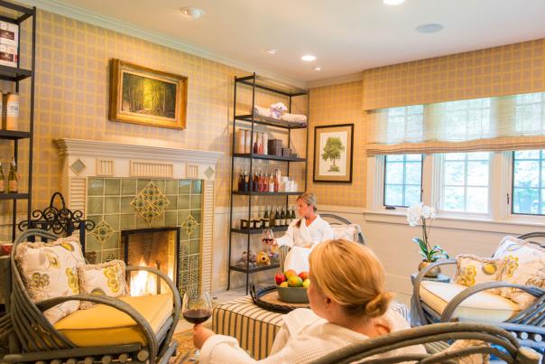 Two ladies in robes sitting in a luxurious sitting room at The Lodge at Glendorn with a lit fireplace. Both women are holding glasses of wine