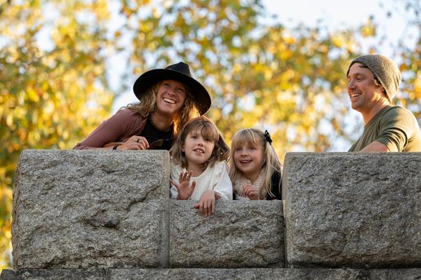 A man and a woman peering over a stone wall with two small girls