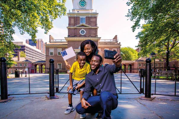 A man posing for a selfie with a woman holding a small American flag and a young boy in front of a historical building
