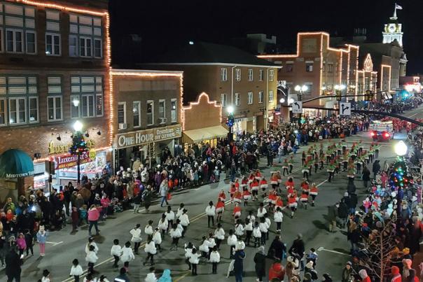 A main street at night with a parade and Christmas lights decorating the town