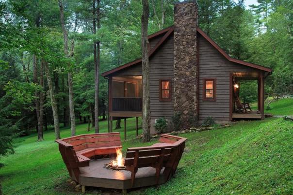 Exterior of a rustic, wood cabin with a fire pit outside and two red benches around it