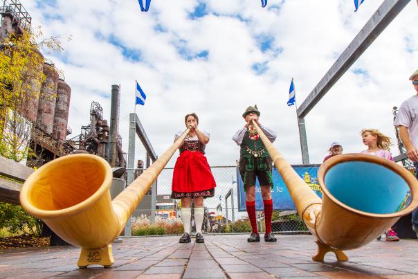 A man and woman in traditional German attire playing large trumpets on a stage