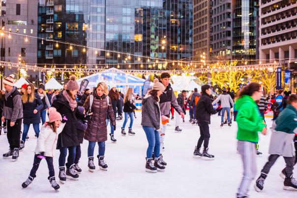People bundled up in winter gear on an outdoor ice skating rink with twinkle lights hanging overhead