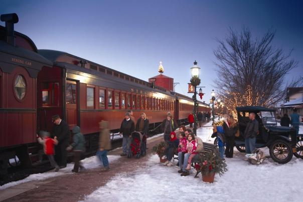 Adults and small children boarding the historic Strasburg Rail Road with snow on the ground and Christmas decorations throughout