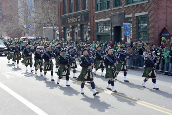 A group of men in Irish attire marching in a street parade with bag pipes