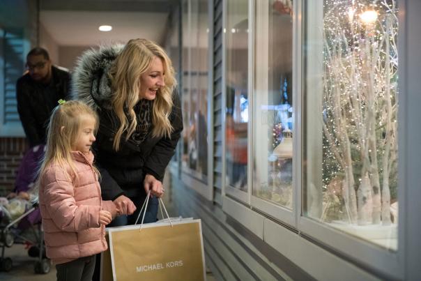 Woman and young girl holding shopping bags and looking into a storefront decorated for the holidays