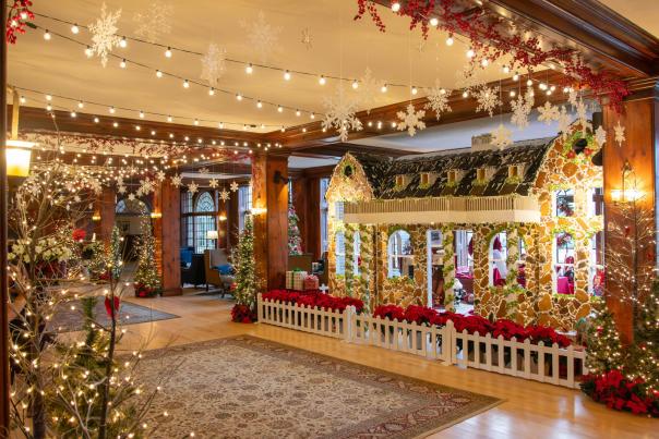Interior of a hotel lobby adorned with holiday lights, pine trees, and a life-size house