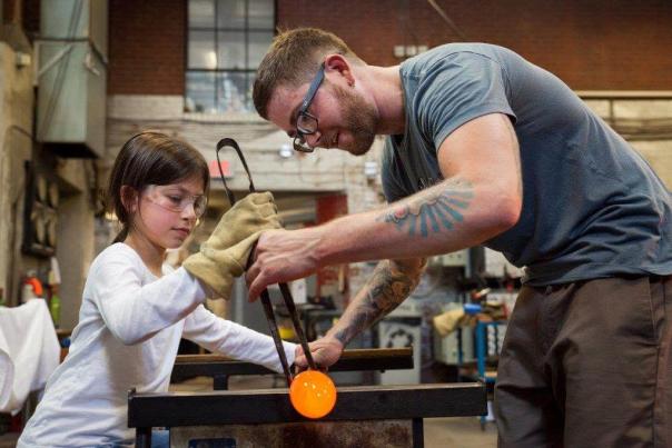 A young girl is being taught to blow glass at the Goggleworks Center for the Arts