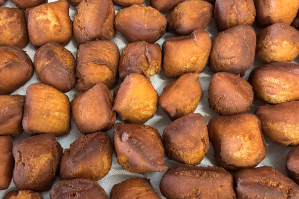 Several dozen fastnachts fresh out of the fryer lined up on a tray ready to be packaged.