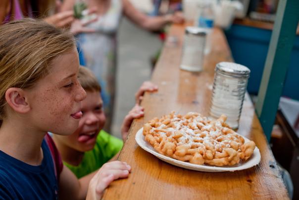 A little girl and a little boy look longingly at a funnel cake.