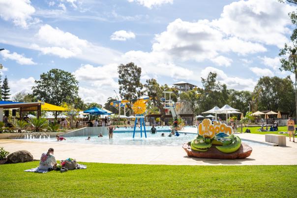 Women sitting on grass in front of Perth's Outback Splash's lagoon pool.