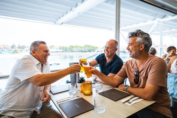 Three men toasting a drink together at a table overlooking the Hillarys Boat Harbour.