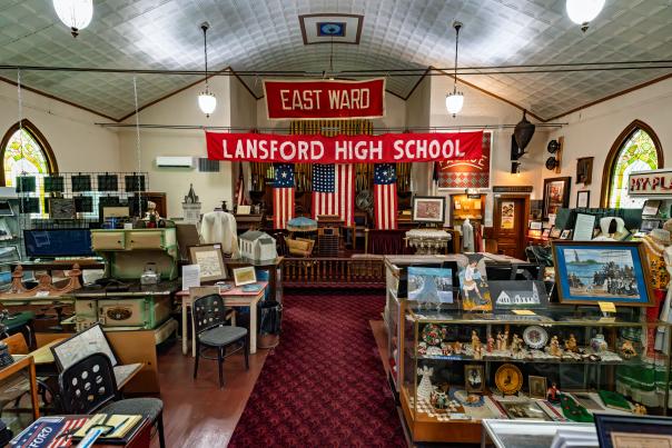 Interior of a historical society museum with glass display cases holding antiques and framed portraits on the walls.