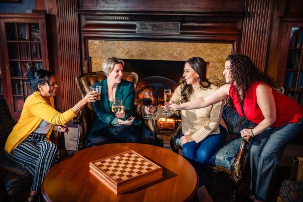 A group of women with wine glasses relax by the fireplace in the Library Lounge at Skytop Lodge in the Pocono Mountains.