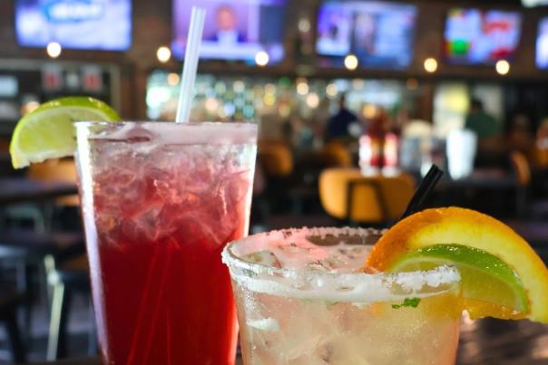 Two Cocktails sitting on a table with four TV screens in the background