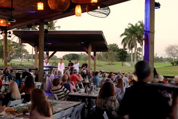 Five well-dressed men, performing on an open-air stage at The Deck @ Galuppi's with the Pompano Beach Golf Course in the background.