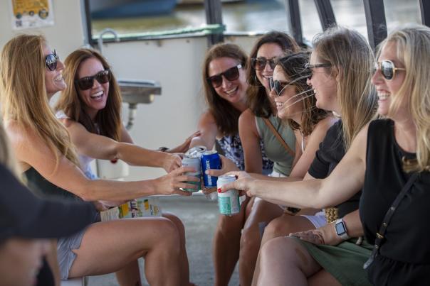 Six ladies toasting with cans of beer and hard seltzer while riding on the Water Taxi.