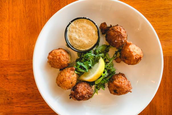 A plate of hushpuppies with sauce, greens, and a lemon is shot from overhead