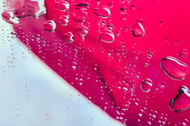 Droplets of water are on a mirror which reflects a pink umbrella