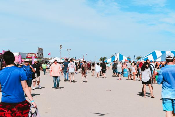 A crowd of people walking along the beach with carnival tents