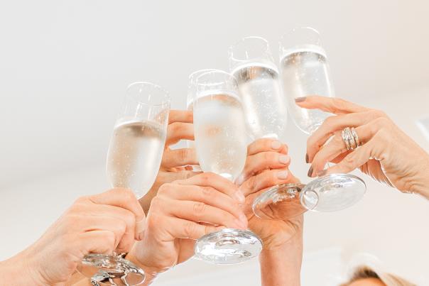 Five peoples hands holding champagne glasses all together the center doing a cheers