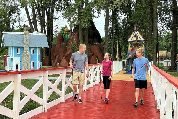 A father and his two teenage children walk along a bridge while holding golf clubs.