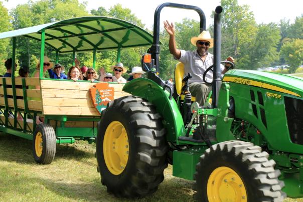 A man drives a green tractor that pulls a trailer full of people.