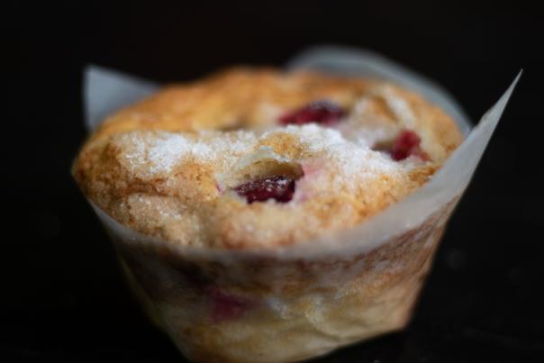 A cranberry muffin with a paper wrapper is behind a black background.