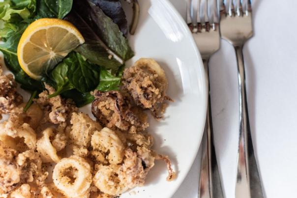 A plate of fried calamari garnished with greens and two forks on the right of the plate.