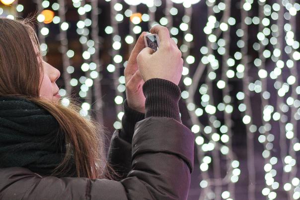 A girl taking a photo of Christmas lights with her cellphone.