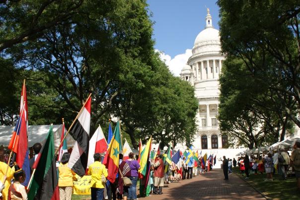 Adults and children line the walkway leading up to the Rhode Island State House holding flags representing various countries.